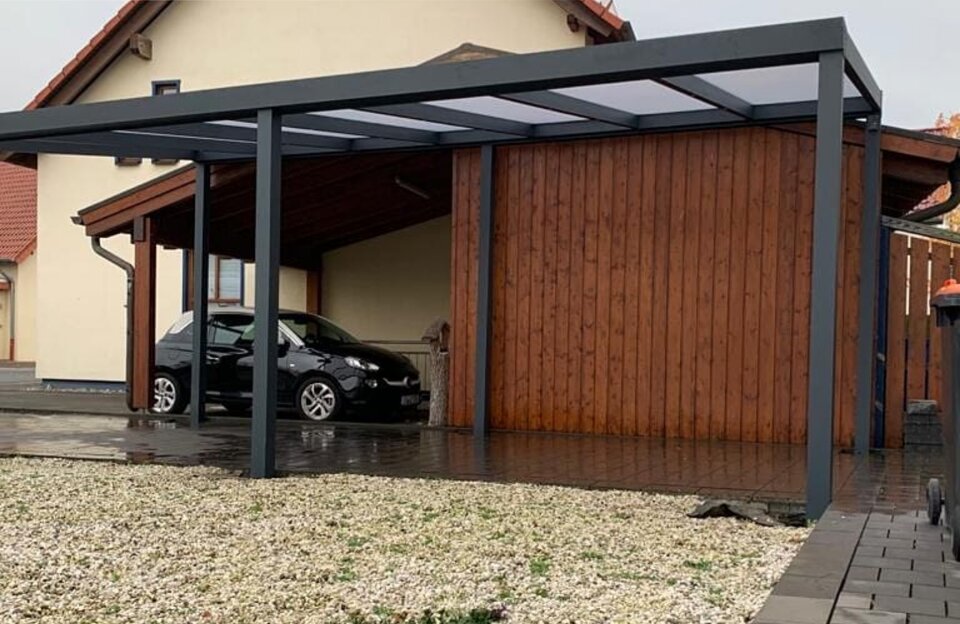 Moderner Carport mit robusten Aluminiumrahmen und transparenten Polycarbonatplatten, neben einem Holzschuppen.